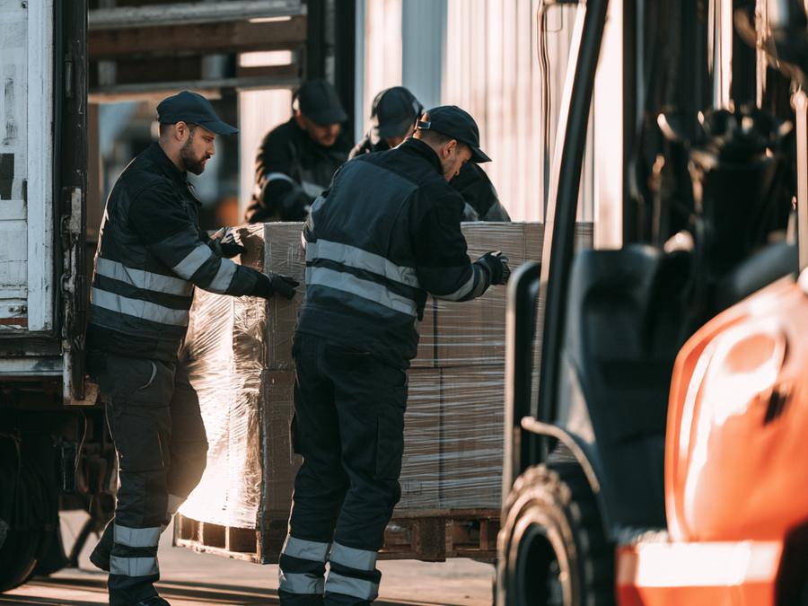Workers loading a shrink-wrapped pallet into a truck at a loading dock